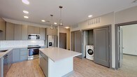 Located at 1005 W Main St in Durham, NC, this contemporary single-floor residence showcases a clean, modern design throughout. The open-concept kitchen serves as the heart of the home, featuring sleek gray cabinetry, quartz countertops, a white subway tile backsplash, stainless steel appliances including a gas range, built-in microwave, and French door refrigerator. A large central island with pendant lighting provides additional prep and seating space. In-unit laundry is conveniently integrated near the kitchen entry. Light wood-look flooring flows seamlessly throughout the entire space, complementing the neutral color palette. The spacious living area is filled with natural light from multiple large windows and includes access to a private balcony. Bedrooms are generously sized, with one featuring a ceiling fan and bright window views, and another connecting directly to a full en-suite bathroom. The bathrooms are well-appointed with gray vanities, quartz countertops, large mirrors, and wood-look flooring. One bathroom includes a soaking tub with subway tile surround, while the primary suite offers access to a walk-in closet with built-in shelving. Recessed lighting throughout enhances the bright, contemporary ambiance of this thoughtfully designed residence.