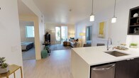 This thoughtfully designed single-floor residence offers a seamless blend of modern style and everyday functionality. The open-concept layout connects the kitchen and living area, creating a bright, airy atmosphere enhanced by light wood flooring throughout. The kitchen is a standout feature, equipped with dark cabinetry, stainless steel appliances including a gas range and French door refrigerator, white quartz countertops, a patterned tile backsplash, and a central island with bar seating illuminated by pendant lighting. The living area is warm and inviting, with sliding glass doors that open onto a private balcony, bringing in natural light and outdoor views. The primary bedroom features soft carpet, a soothing color palette, a large window, and access to a walk-in closet with built-in shelving. A second bedroom provides additional comfort with neutral tones and ample natural light. Two full bathrooms complement the layout — one featuring a dark-cabinetry vanity with built-in shelving, and the other offering a soaking tub with subway tile surround and a minimalist white finish. Throughout, clean lines, recessed lighting, and a cohesive neutral palette create a polished, contemporary living environment.