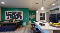 This single-floor residence offers a thoughtfully designed open-concept layout that seamlessly connects the kitchen, dining, and living areas. The kitchen is a standout feature, equipped with modern two-tone cabinetry, a tile backsplash, black appliances including a refrigerator, range, and microwave, and a central island with a white countertop and bar seating for two. Pendant lighting and track lighting illuminate the space, which also includes an in-unit washer and dryer. Bold emerald green accent walls in the open living and dining area add a vibrant pop of color, complemented by light wood-style flooring that runs throughout the main spaces. The living room provides a comfortable retreat with a ceiling fan, wall-mounted TV, built-in shelving, and a sliding glass door that opens to an outdoor balcony, filling the room with natural light. The bedroom features plush carpeting, a ceiling fan, and a window dressed with layered blinds and patterned curtains that invite soft, natural light. The bathroom is finished with dark wood vanity cabinetry, a white countertop, a large mirror with overhead lighting, and a full tub-shower combination with wood-style flooring for a clean, contemporary look.