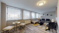 Located in the heart of Cleveland, OH, this well-appointed single-floor unit offers a thoughtfully designed layout that maximizes both comfort and functionality. The entryway greets you with clean lines, neutral-toned walls, and wood-style plank flooring that carries through the main living areas, creating a cohesive and modern aesthetic throughout.

The spacious living area is a standout feature, lined with a bank of large windows dressed with horizontal blinds that frame impressive views of the Cleveland skyline. Natural light fills the room generously, lending an airy, open atmosphere well-suited for both relaxing and entertaining.

The kitchen is efficiently designed with white shaker-style cabinetry, brushed nickel hardware, a deep undermount sink, white countertops, and a full suite of stainless steel appliances including a refrigerator, electric range, dishwasher, and microwave.

The bedroom offers a serene retreat with plush carpeting, cool gray walls, and wide windows that continue the city view theme. The bathroom is tastefully finished with a white vanity, subway-tiled tub and shower surround, brushed nickel fixtures, and dark mosaic tile flooring, striking a clean, contemporary balance. Together, these spaces create a cohesive and inviting urban living environment.