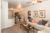 Located in the Antequera neighborhood of Albuquerque, New Mexico, this single-story residence offers a well-designed, open-concept floor plan that connects the living, dining, and kitchen areas seamlessly. The living room is finished with crown molding, a ceiling fan, and plush carpeting, and receives generous natural light through large windows dressed with decorative patterned drapes. Built-in arched niches add architectural character to the walls. The adjacent dining area features wood-style flooring, a modern chandelier, and a louvered closet door. The kitchen is outfitted with rich dark cabinetry, granite-style countertops, and stainless steel appliances including a range with microwave. Both bedrooms are comfortably sized with carpeted floors, natural light, and walk-in or standard closets. The bathrooms mirror each other in finish quality, each offering dark vanity cabinetry, granite countertops, wood-style tile flooring, and a shower-tub combination. Throughout the home, a cohesive neutral color palette creates a warm and inviting ambiance, while consistent finishes across each room contribute to a polished, move-in-ready feel.