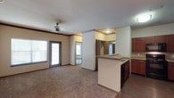 This single-story 2-bedroom, 2-bathroom residence offers a thoughtfully designed open-concept floor plan that maximizes both functionality and comfort. The main living area features warm, neutral-toned carpet, crown molding, and a ceiling fan, creating an inviting atmosphere filled with natural light from large windows and a glass-paneled door that brightens the entire space.

The kitchen is seamlessly integrated into the living area via a peninsula-style breakfast bar with a dark countertop, providing both additional prep space and a casual dining option. Rich, dark wood cabinetry adds warmth and contrast, while hard surface flooring grounds the culinary space with a clean, practical aesthetic. A built-in dishwasher and sink are neatly incorporated into the peninsula layout.

A central hallway connects the living areas to the two bedrooms, one of which is visible with mirrored closet doors that enhance the sense of space. The home's open sightlines from the living room through to the kitchen and hallway create a cohesive and airy feel throughout. Crown molding details and consistent neutral tones tie each area together, lending the home a polished, unified look. This well-appointed residence offers a comfortable and practical living environment with quality finishes at every turn.