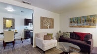 This single-floor residence offers a thoughtfully organized layout that connects key living spaces in a practical and comfortable flow. The living room serves as the heart of the home, featuring warm wood-style flooring, neutral-toned walls, and ample natural light streaming through a large window. The space comfortably accommodates multiple seating arrangements centered around a glass-top coffee table, creating an inviting setting for relaxing or entertaining.

Adjacent to the living area, the kitchen is outfitted with dark espresso cabinetry, granite-style countertops, and standard appliances including a full-size refrigerator. A large window in the kitchen area allows natural light to pour in, offering views of the surrounding greenery. The dining area is a cozy nook featuring a glass-top table and upholstered chairs, complemented by closet storage nearby.

The bedroom offers plush carpeted flooring, a window with vertical blinds overlooking outdoor greenery, and sufficient space for a full furniture suite. The bathroom is clean and functional, featuring a full tub-shower combination with chrome fixtures. Wood-style flooring runs consistently through the main living areas, while the bedroom provides the added comfort of carpet, contributing to a cohesive and well-finished interior throughout.