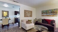 This single-floor residence offers a thoughtfully organized layout that connects key living spaces in a practical and comfortable flow. The living room serves as the heart of the home, featuring warm wood-style flooring, neutral-toned walls, and ample natural light streaming through a large window. The space comfortably accommodates multiple seating arrangements centered around a glass-top coffee table, creating an inviting setting for relaxing or entertaining.

Adjacent to the living area, the kitchen is outfitted with dark espresso cabinetry, granite-style countertops, and standard appliances including a full-size refrigerator. A large window in the kitchen area allows natural light to pour in, offering views of the surrounding greenery. The dining area is a cozy nook featuring a glass-top table and upholstered chairs, complemented by closet storage nearby.

The bedroom offers plush carpeted flooring, a window with vertical blinds overlooking outdoor greenery, and sufficient space for a full furniture suite. The bathroom is clean and functional, featuring a full tub-shower combination with chrome fixtures. Wood-style flooring runs consistently through the main living areas, while the bedroom provides the added comfort of carpet, contributing to a cohesive and well-finished interior throughout.