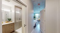 Located at 1110 W Wilson Ave in Chicago's Uptown neighborhood, this single-floor studio showcases a thoughtfully designed open-concept layout that maximizes functionality without sacrificing style. The main living area features exposed concrete ceilings, which lend an industrial character to the space, while light wood-tone flooring adds warmth underfoot. A large floor-to-ceiling window anchors the living and sleeping area, flooding the space with natural light and offering views of the surrounding cityscape.

The sleeping and living zones are seamlessly integrated, with ample room for a full-sized bed and a dedicated seating arrangement. The kitchen is outfitted with flat-front cabinetry in a light wood finish, white quartz countertops, a white subway tile backsplash, stainless steel appliances including a gas range and built-in microwave, and a matte black faucet over an undermount sink — combining modern aesthetics with practical functionality.

The bathroom features tile flooring, a floating vanity with wood-toned cabinetry and a white countertop, a large mirror, and a separate glass-enclosed shower with tile surround. A louvered door leads between the hallway and living area, adding a clean architectural detail. Overall, the space presents a cohesive, contemporary design well-suited for urban living.