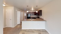 This single-floor residence offers a thoughtfully designed layout with a clean, neutral aesthetic throughout. The kitchen serves as a central hub, featuring rich dark cabinetry, laminate countertops, a peninsula with a double sink, and pendant lighting that adds a warm, inviting glow. Black appliances, including a refrigerator, range, and over-the-range microwave, are seamlessly integrated into the cabinetry. Wood-look flooring runs through the kitchen and flows into the adjacent living area, which transitions into soft carpeting.

The bedrooms are finished with plush carpet, neutral-toned walls, and window blinds that allow for natural light control. One bedroom includes a reach-in closet with a double hanging rod, providing practical storage. The remaining bedroom offers a similarly comfortable and adaptable space.

Two full bathrooms mirror each other in style, each featuring dark espresso-toned vanity cabinetry, stone-look countertops, a single basin sink, and wood-look tile flooring. One bathroom includes a shower-tub combination, while the other offers a walk-in shower stall. Both are accented with modern light bars above framed mirrors, creating a bright and functional environment. The overall design is cohesive, practical, and move-in ready.