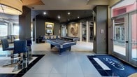Located at 9663 E Lincoln Ave in Lone Tree, Colorado, this single-floor amenity space combines contemporary design with a diverse range of functional areas. The layout is expansive and open, with light-toned large-format tile flooring flowing throughout, unifying the various zones into a cohesive environment.

The entrance area features floor-to-ceiling glass-walled office suites with aluminum framing, offering transparency while maintaining private workspaces. Each glass-enclosed office is outfitted with warm wood cabinetry and built-in shelving, providing a polished, professional atmosphere.

A kitchenette serves as a practical hub within the space, highlighted by bold crimson glass backsplash panels, rich zebrawood cabinetry, black granite countertops, and stainless steel appliances, delivering a striking visual contrast.

The dining area is bathed in natural light through oversized windows framed by sheer drapery, offering views of the surrounding streetscape. Adjacent to this is a generously sized recreation lounge featuring two full-size pool tables set against dark-painted walls accented by dramatic decorative artwork. Wall-mounted televisions, built-in lounge seating with accent pillows, and recessed lighting complete the entertainment atmosphere. Large glass doors connect this area to an outdoor patio, enhancing the overall sense of openness.