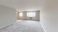 This single-floor unit is designed with a practical, straightforward layout that maximizes usable space throughout. The generously sized living area serves as the heart of the unit, featuring neutral-toned wall-to-wall carpeting, a ceiling fan, and multiple windows fitted with vertical blinds that allow ample natural light to filter in. Baseboard heating runs along the exterior walls, complemented by wall-mounted air conditioning units, ensuring year-round climate comfort.

The galley-style kitchen is outfitted with warm wood cabinetry, white countertops, tile flooring, and a full suite of white appliances including a gas range and overhead microwave. A sliding door leads to an adjacent storage or pantry space, adding convenient organization options.

The bedrooms are carpeted and neutrally finished, each equipped with individual window units and baseboard heaters. One bedroom features dual bifold closets, offering substantial storage. Additional rooms provide ample space for flexible use.

Two bathrooms serve the unit: one includes a tub-shower combination with distinctive light blue tile surround and tile flooring, while the second features a standalone shower enclosure accented by classic pink tile walls. Both bathrooms maintain a clean, functional character throughout.
