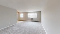 This single-floor unit is designed with a practical, straightforward layout that maximizes usable space throughout. The generously sized living area serves as the heart of the unit, featuring neutral-toned wall-to-wall carpeting, a ceiling fan, and multiple windows fitted with vertical blinds that allow ample natural light to filter in. Baseboard heating runs along the exterior walls, complemented by wall-mounted air conditioning units, ensuring year-round climate comfort.

The galley-style kitchen is outfitted with warm wood cabinetry, white countertops, tile flooring, and a full suite of white appliances including a gas range and overhead microwave. A sliding door leads to an adjacent storage or pantry space, adding convenient organization options.

The bedrooms are carpeted and neutrally finished, each equipped with individual window units and baseboard heaters. One bedroom features dual bifold closets, offering substantial storage. Additional rooms provide ample space for flexible use.

Two bathrooms serve the unit: one includes a tub-shower combination with distinctive light blue tile surround and tile flooring, while the second features a standalone shower enclosure accented by classic pink tile walls. Both bathrooms maintain a clean, functional character throughout.