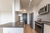 Located at 77 Parkwoods Village Dr in Toronto, this two-bedroom, one-bathroom unit offers a well-organized layout with light wood flooring throughout and a clean, modern aesthetic. The open-concept living, dining, and kitchen area forms the heart of the unit, providing a versatile and connected space. The kitchen is outfitted with white shaker-style cabinetry, a quartz countertop peninsula with a double undermount sink, stainless steel appliances, and a herringbone tile backsplash that adds a refined touch. Both bedrooms are bright and well-proportioned, featuring large windows that allow generous natural light to fill the rooms, along with elevated views of the Toronto skyline and surrounding greenery. The bathroom is finished with white subway tile in the tub surround, a vanity with chrome fixtures, and neutral floor tiles. A hallway connects the rooms efficiently, maintaining a logical and functional flow. The unit also includes a balcony that extends the living space outdoors, offering sweeping elevated views of the city and tree-lined streets below. The overall palette of white walls, light flooring, and contemporary finishes creates a bright, clean, and inviting atmosphere throughout.