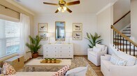 Located at 120 Buck Island Rd in Bluffton, SC, this well-appointed two-story home offers three bedrooms and three bathrooms across two thoughtfully designed floors. The main level features an open-concept living, dining, and kitchen area filled with natural light from large windows dressed in sheer white curtains. The kitchen stands out with crisp white shaker cabinetry, quartz countertops, a herringbone tile backsplash, stainless steel appliances, and warm hardwood-style flooring. Crown molding and neutral warm-toned walls carry throughout the main level, lending a cohesive, polished feel. The dining area accommodates an intimate table setting bathed in natural light, while the living room features a shiplap accent wall and coastal-inspired décor. A hallway connects the entry to the main living spaces, complemented by an attached garage with an automatic opener. Upstairs, the upper level hosts all three bedrooms, including a generously sized primary bedroom with carpet flooring, crown molding, a ceiling fan, a dedicated closet, and an en-suite bathroom featuring a glass-enclosed shower and white vanity cabinetry. The additional bedrooms are comfortably sized with plush carpet and natural light. A nautical-themed powder bath with a sloped ceiling adds a charming coastal touch.