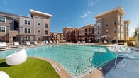 This two-story residential community is centered around a generously sized resort-style pool courtyard that serves as the focal point of the outdoor amenity space. The pool features clearly marked depth indicators, a pool lift for accessibility, and designated swim lanes, underscoring the facility's commitment to inclusive design. Surrounding the pool is a spacious sun deck furnished with lounge chairs and shade umbrellas, providing ample space for relaxation.

Adjacent to the pool deck is a well-maintained turf lawn area appointed with contemporary pod-style seating, offering a casual gathering space distinct from the poolside lounging area. A covered pergola structure anchors one side of the courtyard, providing shaded seating and an outdoor living environment suitable for multiple uses.

The multi-building architecture features a modern design blending brick and neutral-toned exterior finishes across several interconnected structures. Ground-level covered entries with tile flooring and crown molding detailing provide sheltered access to individual units, with iron railings and gated access points framing the courtyard perimeter. The open-sky orientation of the courtyard ensures abundant natural light throughout the day, creating a bright and inviting outdoor atmosphere consistent with the community's contemporary aesthetic.