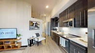 Located at 451 2nd Ave S in the heart of downtown Saint Petersburg, Florida, this contemporary single-floor residence showcases a sleek, modern design with cohesive finishes throughout. The open-concept layout seamlessly connects the kitchen and living area, creating an efficient and stylish space. The kitchen is outfitted with dark wood-grain cabinetry extending to the ceiling for ample storage, stainless steel appliances including a refrigerator, range, and microwave, light countertops, and a subway tile backsplash. Light-toned tile flooring runs throughout the main living areas, adding a clean, airy aesthetic. The living room benefits from large windows that invite natural light and offer views of the surrounding downtown cityscape, with elevated ceilings enhancing the sense of openness. The bedroom is a comfortable retreat featuring plush carpeting, a walk-in closet with built-in shelving and hanging space, and tasteful wall decor. The bathroom maintains the unit's modern palette with matching dark cabinetry, a tub-shower combination, and tile flooring that mirrors the rest of the home. Ceiling fans are present in the living and sleeping areas for year-round comfort. The overall ambiance is polished and contemporary, ideal for urban living in vibrant downtown St. Petersburg.
