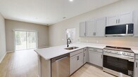 Located at 5790 Stockport St in Riverview, FL, this single-floor, 2-bedroom, 1-bathroom residence offers a clean, modern aesthetic throughout. Light wood-style flooring flows consistently across all rooms, complemented by neutral greige walls and crisp white trim, creating a bright and cohesive interior.

The combined kitchen and living area serves as the heart of the home. The kitchen is well-appointed with gray shaker-style cabinetry, white countertops, and a full suite of stainless steel appliances including a gas range, over-the-range microwave, and refrigerator. The adjacent living room features a sliding glass door fitted with vertical blinds, providing direct outdoor access and filling the space with natural light.

Both bedrooms are comfortably sized, each featuring a ceiling fan, windows with blinds for natural light, and bi-fold closet doors offering generous storage. The primary bedroom is a well-proportioned retreat with ample room for furnishings.

The full bathroom is finished with gray vanity cabinetry, a white countertop, a large mirror, and a walk-in shower enclosed by a sleek black-framed glass door. A hallway connects the main living areas to the bedrooms and bathroom, ensuring a practical and efficient layout throughout this well-maintained Riverview residence.