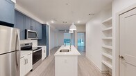 Located at 55 Romney St in Charleston's historic 29403 zip code, this thoughtfully designed one-bedroom, one-bathroom unit offers a modern aesthetic throughout. Light wood-look flooring flows seamlessly across the single-level floor plan, creating a cohesive and contemporary feel.

The kitchen serves as the heart of the space, boasting bold slate-blue upper cabinetry contrasted by crisp white lower cabinets and quartz countertops. A center island with an undermount sink and pendant lighting provides additional prep and seating space, while stainless steel appliances — including a refrigerator, range, microwave, and dishwasher — complete the chef-ready setup. Open built-in shelving adds both storage and visual interest adjacent to the kitchen.

The living area is bright and open, featuring a ceiling fan and views toward large windows that invite natural light. The bedroom offers an intimate retreat with exposed concrete ceiling accents, large floor-to-ceiling windows, and light-filled ambiance.

The bathroom is well-appointed with a soaking tub and shower combo, a wide vanity with dual sinks, quartz countertops, and a large framed mirror. A dedicated laundry closet with a stacked Whirlpool washer and dryer adds everyday convenience to this efficiently designed Charleston residence.