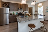 Located at 9635 Westland Cove Way in Knoxville, Tennessee, this single-floor residence offers a thoughtfully designed layout with modern finishes throughout. The entryway opens into a bright, open-concept living area with wood-look flooring that flows seamlessly into the kitchen and living spaces. The kitchen is a standout feature, showcasing dark espresso cabinetry, granite countertops, stainless steel appliances including a refrigerator, range, and microwave, a built-in wine rack, and a large island with pendant lighting — ideal for both cooking and entertaining. The living room is well-lit and open, offering a comfortable, inviting atmosphere. The residence includes multiple bedrooms, each carpeted and featuring ceiling fans or windows that bring in natural light. One bedroom includes a ceiling fan with light fixture, while another offers a window with views to the outside. The bathrooms are finished with granite vanity tops and dark wood cabinetry; one features a tub-shower combo and another a sleek walk-in shower with a black-framed glass door. A dedicated laundry room houses a full-size Whirlpool washer and dryer set with overhead shelving for added storage convenience.