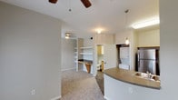 This single-floor residential unit offers a thoughtfully designed layout that balances functionality and comfort. The open-concept kitchen is equipped with light maple cabinetry, dark laminate countertops, stainless steel appliances including a refrigerator, range, and microwave, and a double-basin sink. Wood-look flooring runs throughout the kitchen and hallway areas, lending a warm, cohesive feel to the space.

Adjacent to the kitchen, a dedicated laundry closet houses a stacked washer and dryer unit, adding in-unit convenience. The living area features plush wall-to-wall carpeting and ceiling fans, creating a comfortable and relaxed atmosphere. Built-in open shelving and a built-in desk nook provide practical storage and workspace solutions within the main living space.

The bathroom is outfitted with a full soaking tub and shower combination finished with white subway tile, wood-look flooring, and light maple vanity cabinetry topped with a countertop sink and mirror.

The bedroom is generously proportioned, featuring soft carpeting, a ceiling fan, and multiple windows that allow natural light to fill the room. A walk-in closet offers ample storage, while French doors open directly onto a private balcony, providing an inviting outdoor retreat with views of the surrounding exterior.