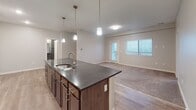 This single-floor unit is designed with a clean, contemporary aesthetic and a practical open-concept layout. The kitchen serves as the focal point of the main living area, anchored by a large island with a dark stone countertop, an undermount sink, and pendant lighting overhead. Dark-stained cabinetry lines the kitchen walls, complemented by a full suite of stainless steel appliances including a refrigerator, range, and microwave. Light wood-style flooring extends throughout the kitchen and main living area, which flows seamlessly into a spacious carpeted living room. A glass-paneled door provides natural light and outdoor access from the living area.

The bedrooms are carpeted and well-lit by large windows with horizontal blinds that offer views of the surrounding area. The primary bedroom features a ceiling fan and dual windows, enhancing both ventilation and natural light. Two bathrooms serve the unit — one with a walk-in shower stall and the other with a full soaking tub and shower combination, both finished with light wood-look flooring and chrome fixtures. A dedicated laundry room accommodates a full-size washer and dryer with an overhead wire shelf for additional storage. The overall ambiance is modern, clean, and move-in ready.