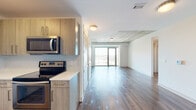 This single-floor residence showcases a thoughtfully designed open-concept layout that seamlessly connects the kitchen and living areas. The kitchen is outfitted with light wood cabinetry featuring brushed gold hardware, white quartz countertops, a geometric mosaic tile backsplash, and a full suite of stainless steel appliances including a range, built-in microwave, and dishwasher.

The living area transitions naturally from the kitchen, characterized by wide-plank hardwood flooring and a striking exposed concrete ceiling detail that adds an industrial contrast to the otherwise clean, contemporary aesthetic. Floor-to-ceiling sliding glass doors flood the space with natural light and provide direct access to a private balcony with open city views.

The bedrooms continue the modern design language with plush carpeting, exposed concrete ceilings, large sliding glass doors to balcony access, and generously sized walk-in closets with built-in shelving systems.

The bathrooms are finished with marble-style porcelain tile throughout. The primary bath includes a glass-enclosed walk-in shower with large-format tile surround, while the secondary bath features a soaking tub with a matching tiled surround and a curved shower rod.