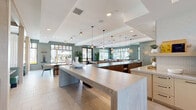 Located at 1464 Laurel Sound Ln in Sanford, Florida, this expansive single-floor community clubhouse offers a generously sized, thoughtfully designed space for socializing, working, and recreation. The interior is defined by soaring double-height ceilings in the entrance area, exposed wood beam accents, and large black-framed windows that flood the space with natural light and provide views of the surrounding community and outdoor greenery.

The open-plan layout flows seamlessly between distinct zones. A co-working area near the entrance features structural wood columns and ample desk space. Adjacent to it, a fully equipped coffee and refreshment bar offers light cabinetry, quartz countertops, and a commercial beverage station beneath a dramatic skylight. A long island with bar seating and pendant lighting anchors the central social hub, complemented by a large-screen TV and display shelving.

The dining and lounge areas are elegantly appointed, with leather banquette seating, statement pendant chandeliers, and floor-to-ceiling windows. A cozy nook with green upholstered benches and a dark wood table offers a more intimate retreat. The game room features a billiards table, potted fiddle-leaf fig trees, and direct access to the outdoor pool area through glass-paned French doors. Throughout, sage green accent walls, light stone tile flooring, and curated decor create a cohesive, contemporary Florida ambiance.