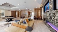 Located at 2031 Maywill St in Richmond, Virginia, this single-floor community amenity space combines contemporary design with practical resident-focused features throughout its well-appointed areas. The welcoming lobby sets the tone with eye-catching geometric patterned tile flooring, globe pendant lighting, warm wood-clad columns, and a built-in mailroom with both individual mailboxes and package lockers. A convenient pet-washing station and luggage carts are also accessible from this entry area. The leasing and co-working area features a stunning live-edge marble conference table surrounded by upholstered chairs, set beneath a tray ceiling with accent lighting, complemented by teal-toned walls and decorative wall art. The spacious lounge serves as the heart of the amenity space, with vertical wood slat dividers creating visual separation between zones. A dramatic marble-clad feature wall anchors the room, housing a linear electric fireplace flanked by two large-screen televisions. The community kitchen is a standout, boasting a bold emerald green herringbone tile backsplash, warm wood cabinetry, quartz countertops, a large center island with bar seating, stainless steel appliances, and modern pendant lighting. Natural light flows throughout from generously sized windows, creating an inviting and cohesive atmosphere across all areas.