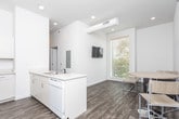 Located in Clarksville, Tennessee, this single-floor unit offers a practical and well-organized layout designed to accommodate multiple occupants. The interior features a clean, modern aesthetic with white walls and a neutral color palette throughout.

The kitchen serves as a functional hub of the unit, featuring white cabinetry, a peninsula with an integrated sink, a full-size refrigerator, and a range. A stacked washer and dryer unit is conveniently positioned adjacent to the kitchen, adding everyday practicality.

The private sleeping areas are carpeted with a patterned tile-style carpet and include natural light from windows with blinds. Each room is furnished with a bed frame and mattress, providing a ready-to-use living space. A dedicated desk area is also present in at least one of the rooms.

The common living area features light wood-tone flooring and is furnished with a gray sofa, offering a comfortable shared space. The bathroom is finished with wood-look vinyl flooring, a white vanity with storage cabinetry, and a toilet, maintaining the consistent clean and modern style found throughout the unit. Recessed lighting and chrome hardware details contribute to the overall polished presentation of this multi-room Clarksville residence.