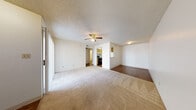 This single-floor residential unit offers a functional and well-organized layout designed for comfortable everyday living. The open living area is generously sized, featuring plush wall-to-wall carpeting, a textured ceiling, and a ceiling fan with integrated light fixture. The space flows naturally toward a dining or flex area finished with wood-look hard flooring, providing a clear visual and material transition between zones. A large sliding glass door allows natural light to fill the living area.

The galley-style kitchen is efficiently designed with warm wood cabinetry lining both walls, light stone-tone countertops, a double-basin sink, and black appliances including a range and refrigerator. A pass-through opening connects the kitchen to the adjacent living and dining space, enhancing the sense of openness.

The bedroom is carpeted and well-proportioned, featuring a large window that brings in natural light and a sliding mirrored closet door that adds depth to the room. An additional carpeted room with a front entry door and a side window functions as a secondary bedroom or flex space, complete with a ceiling fan and access to a folding-door closet.

The bathroom includes a wood-tone vanity with stone-look countertop, a wide mirror with overhead lighting, hardwood-style flooring, and a dedicated in-unit stacked washer and dryer — a practical and convenient feature. Throughout, the unit maintains a clean, neutral palette that offers a versatile canvas for personalization.