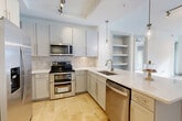 Located at 25 W Tremont Ave in Charlotte's vibrant Dilworth neighborhood, this well-appointed 2-bedroom, 2-bathroom residence offers a thoughtfully designed single-level layout. The open-concept kitchen and living area serves as the heart of the home, where warm hardwood floors extend throughout the main living space. The kitchen is outfitted with stainless steel appliances—including a double oven range, built-in microwave, dishwasher, and French door refrigerator—complemented by a herringbone tile backsplash, gray shaker cabinetry, quartz countertops, and a peninsula island with pendant lighting. A tray ceiling with track lighting adds architectural character overhead, while built-in shelving provides additional display and storage space. The primary bedroom features plush carpeting, a ceiling fan, and sliding glass doors opening to a private balcony with city views. The second bedroom also offers carpeted flooring and generous natural light. Both bathrooms are finished with travertine tile flooring, and the primary bath includes a dual-sink vanity with a framed mirror and brushed nickel fixtures. A dedicated laundry room with a full-size washer and dryer adds everyday convenience, rounding out this well-equipped urban residence.