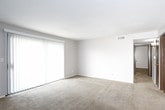 This single-floor unit offers a practical and functional layout spread across several well-defined rooms. The living area is generously sized, featuring neutral-toned carpet flooring, light gray walls, and a textured ceiling. A large sliding glass door fitted with vertical blinds floods the space with natural light and provides direct access to an outdoor area, creating an open and airy atmosphere.

The kitchen is efficiently designed with dark espresso-toned cabinetry spanning both upper and lower sections, offering ample storage. It includes a full-size refrigerator, a white electric range with an overhead microwave, a double-basin sink, and laminate countertops. Rich wood-look flooring anchors the kitchen, providing a clean contrast to the darker cabinetry.

The unit features multiple bedrooms, each finished with wall-to-wall carpet and neutral gray walls under textured ceilings. One bedroom includes a set of large dark-paneled sliding closet doors that add a bold design element, while other bedrooms feature windows dressed with blinds that bring in natural light. The floor plan, as visible in the dollhouse view, reveals a compact and efficiently organized layout with clear separation between living, sleeping, and kitchen spaces, and multiple interior doors providing privacy throughout.