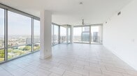 Located on the 40th floor at 215 North Pine Street in uptown Charlotte, this high-rise residence offers three bedrooms and three bathrooms across a generously proportioned single-level layout. Floor-to-ceiling glass walls flood the open living area with natural light while framing dramatic, panoramic views of the Charlotte skyline and surrounding cityscape. Light-toned porcelain tile flows throughout the main living spaces, complementing the bright, airy aesthetic.

The open-concept kitchen is a standout feature, appointed with grey shaker cabinetry, gold hardware, a large center island with a quartz countertop, a gold-tone faucet, a marble-style backsplash, stainless steel appliances including a double wall oven, and a built-in wine cooler. Pendant lighting above the island adds a refined touch.

The bedrooms are well-proportioned, featuring light hardwood flooring, ceiling fans, and direct balcony access with sweeping skyline views. The spacious primary bedroom includes its own access to outdoor space. The primary bathroom is elegantly finished with full marble-style wall tile, a glass-enclosed shower, a soaking tub, and polished gold fixtures throughout. Additional bathrooms maintain a clean, modern palette with white cabinetry and gold accents. Two closets and two hallways complete the layout.