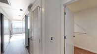 Located on the 12th floor at 830 Eddy Street in San Francisco's Tenderloin neighborhood, Unit 1204 is a modern, single-level residence with a clean, contemporary design throughout. The open-concept living and kitchen area is bathed in natural light, courtesy of large floor-to-ceiling windows that frame striking panoramic views of the San Francisco skyline and surrounding hills. Flooring transitions between light wood-tone and dark hardwood, adding visual contrast and warmth to the interior.

The kitchen is thoughtfully designed with sleek white cabinetry extending to the ceiling, providing ample storage. A full suite of stainless steel appliances — including a refrigerator, range, built-in microwave, and dishwasher — complements the bright white quartz countertops and subway tile backsplash. An interior glass partition wall adds an architectural element that allows light to flow between the kitchen and living areas.

The bathroom features a white vanity with an undermount sink, quartz countertop, large mirror, and chrome fixtures, maintaining the unit's clean, minimalist aesthetic. The bedroom is generously sized with multiple windows offering abundant natural light and open city views. A louvered sliding closet door and a smart thermostat panel are among the practical details found in the hallway. The overall ambiance is bright, airy, and modern.
