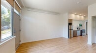 This efficiently designed single-floor unit offers a clean, contemporary aesthetic throughout. The open-concept living area is finished with light-toned hardwood-style flooring and crisp white walls, creating a bright and airy atmosphere. A large window and glass sliding door allow natural light to fill the space while offering views of surrounding greenery, enhancing the overall sense of openness.

The kitchen is seamlessly integrated into the main living area and features stainless steel appliances, including a refrigerator, range, and dishwasher, complemented by warm wood-toned cabinetry and recessed lighting above.

The sleeping area includes a built-in closet with sliding doors and adjustable shelving, providing practical and organized storage. The bathroom is well-appointed with a tiled walk-in shower enclosed by a glass door, wood-style flooring, and a dedicated nook housing a stacked washer and dryer unit — a convenient in-unit laundry solution.

Throughout the space, a consistent neutral color palette, modern finishes, and clean lines contribute to a cohesive and functional living environment. The layout makes efficient use of every square foot, offering a comfortable and well-equipped space suitable for everyday living.