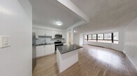 Located at 545-565 Belmont Ave W in Kitchener, Ontario, this well-appointed 4-bedroom, 1-bathroom unit offers a thoughtfully designed single-floor layout with a clean, modern aesthetic throughout. Light wood laminate flooring runs continuously across the living spaces, creating a warm and cohesive feel.

The open-concept kitchen and living area serves as the heart of the unit. The kitchen is outfitted with crisp white cabinetry, a subway tile backsplash, dark countertops, stainless steel appliances including a refrigerator, dishwasher, electric range, and built-in microwave, as well as a central island ideal for meal preparation or casual dining. The expansive living area benefits from a wide, curved bay window that invites abundant natural light and provides views of the surrounding neighbourhood.

The four bedrooms are bright and versatile, each featuring light wood flooring, white walls, and individual windows with outdoor views. The primary bedroom includes a full-width mirrored sliding closet, maximizing both storage and the sense of space. The shared bathroom is finished with large-format floor tiles, a dark wood vanity with a white countertop, subway tile surround on the tub-shower combination, and contemporary light fixtures. A dedicated closet provides additional storage within the unit.