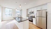 Located at 10 Seventh St W in the heart of downtown Cincinnati, this thoughtfully designed one-bedroom, one-bathroom residence offers a clean, contemporary aesthetic across a single floor. The open-concept kitchen and living area serves as the centerpiece of the unit, featuring a sleek island with a dark granite countertop, an undermount sink, and pendant lighting overhead. The kitchen is outfitted with white shaker-style cabinetry, a subway tile backsplash, and a full suite of stainless steel appliances, including a refrigerator, range, and microwave. Warm hardwood-style flooring runs throughout, complementing the crisp white walls and recessed lighting. Large windows in the living area and bedroom invite abundant natural light and frame views of the surrounding Cincinnati skyline. The bedroom is a well-proportioned retreat featuring a double-door closet and additional closet storage accessible via the hallway. The bathroom is finished with an elegant dark granite vanity top, white shaker cabinetry, a framed rectangular mirror, a stylish multi-bulb light fixture, and distinctive geometric-patterned tile flooring. With four closets total, storage is plentiful throughout. The unit's modern finishes, efficient layout, and prime urban location make it a refined and functional living space.