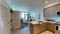 Located on West Pico Boulevard in Los Angeles, this contemporary single-floor residence offers a thoughtfully designed open layout with high-end finishes throughout. The kitchen serves as a central hub, featuring flat-front cabinetry in warm taupe tones, a large island with a undermount sink and stainless steel dishwasher, and a full suite of stainless steel appliances including a range, built-in microwave, and refrigerator. Light wood-style flooring flows seamlessly into the living area, where floor-to-ceiling black-framed glass doors open onto a private balcony showcasing sweeping panoramic views of the Los Angeles skyline. The living space is bright and airy, benefiting from abundant natural light. Two well-appointed bedrooms each feature textured accent walls, large windows framing city views, and ample natural light. The primary bedroom includes access to a spacious en-suite bathroom outfitted with large-format tile flooring, a dual-sink vanity with illuminated mirrors, and a glass-enclosed walk-in shower. A generous walk-in closet with wrap-around shelving and hanging rods provides excellent storage. An in-unit washer and dryer adds everyday convenience to this polished and modern Los Angeles residence.
