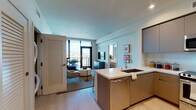 Located on West Pico Boulevard in Los Angeles, this contemporary single-floor residence offers a thoughtfully designed open layout with high-end finishes throughout. The kitchen serves as a central hub, featuring flat-front cabinetry in warm taupe tones, a large island with a undermount sink and stainless steel dishwasher, and a full suite of stainless steel appliances including a range, built-in microwave, and refrigerator. Light wood-style flooring flows seamlessly into the living area, where floor-to-ceiling black-framed glass doors open onto a private balcony showcasing sweeping panoramic views of the Los Angeles skyline. The living space is bright and airy, benefiting from abundant natural light. Two well-appointed bedrooms each feature textured accent walls, large windows framing city views, and ample natural light. The primary bedroom includes access to a spacious en-suite bathroom outfitted with large-format tile flooring, a dual-sink vanity with illuminated mirrors, and a glass-enclosed walk-in shower. A generous walk-in closet with wrap-around shelving and hanging rods provides excellent storage. An in-unit washer and dryer adds everyday convenience to this polished and modern Los Angeles residence.