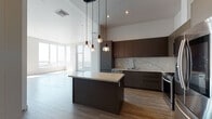 Located in the heart of Downtown Los Angeles at 1133 S Hope St, this contemporary single-floor residence offers a refined urban living experience defined by clean lines and high-end finishes. The open-concept kitchen is a standout centerpiece, showcasing flat-front cabinetry in rich dark and warm gray tones, a striking marble-veined quartz island with pendant lighting overhead, a matching backsplash, and a full suite of stainless steel appliances including a gas range and French door refrigerator. Wide-plank wood-style flooring flows throughout the living areas, complementing the bright, neutral palette of the space. Floor-to-ceiling windows flood the living room with abundant natural light and frame sweeping panoramic views of the Los Angeles skyline, creating a dramatic sense of openness and elevation. The bedrooms are generously proportioned with crisp white walls and ample natural light. The primary bathroom features a dual-sink vanity with wood cabinetry, quartz countertops, a large wall mirror, and a glass-enclosed walk-in shower with tile surround. Additional bathrooms include a soaking tub with tiled surround and a powder room with textured tile accent wall. The unit's overall design exudes a polished, modern aesthetic well-suited to urban living.