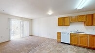 This single-story, 3-bedroom, 2-bathroom home offers a practical and functional layout designed to maximize every square foot of its compact footprint. The open-concept living and kitchen area forms the heart of the home, where warm honey-toned oak cabinetry lines the kitchen walls, providing ample storage. The kitchen is fully equipped with a white appliance suite including a refrigerator, electric range, dishwasher, and a double sink, all set atop tile flooring in a neutral stone-like pattern. The living area flows seamlessly from the kitchen, featuring plush carpeting and a sliding glass door with vertical blinds that invites natural light and provides access to the outdoors. A connecting hallway, accented with an arched architectural detail, links the living space to the private quarters. Each of the three bedrooms is carpeted and features six-panel closet doors with built-in hanging rods. The primary bedroom offers a generous footprint with room for a full furniture arrangement. Both bathrooms are finished with matching tile flooring; one includes a walk-in shower stall, while the other is fitted with a toilet and towel bar. The overall aesthetic is clean, neutral, and move-in ready.