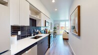 Located on the sixth floor at 8460 164th Ave NE in Redmond, WA, this thoughtfully designed two-bedroom, one-bathroom unit makes efficient use of its compact footprint. The layout flows from a well-appointed galley kitchen through to a comfortable living area, connected by light wood-tone flooring throughout.

The kitchen is a standout feature, showcasing two-tone cabinetry with crisp white upper cabinets and dark lower cabinets, paired with a striking navy hexagonal tile backsplash. Stainless steel appliances and a clean white countertop complete the contemporary look.

The living room benefits from large, floor-to-ceiling windows that flood the space with natural light and frame elevated views of the surrounding Redmond cityscape and greenery — a notable highlight of this sixth-floor position.

Both bedrooms are cozy and efficiently laid out, with the primary bedroom featuring a closet and ample wall space. A sliding barn door adds a stylish, space-conscious touch to the hallway transition. The shared bathroom is clean and modern, featuring a dark wood vanity with an undermount sink, wood-look flooring, and a bright, open layout.

Throughout the unit, white walls and recessed lighting create a bright, neutral backdrop that enhances the sense of space.