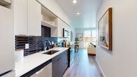 Located on the sixth floor at 8460 164th Ave NE in Redmond, WA, this thoughtfully designed two-bedroom, one-bathroom unit makes efficient use of its compact footprint. The layout flows from a well-appointed galley kitchen through to a comfortable living area, connected by light wood-tone flooring throughout.

The kitchen is a standout feature, showcasing two-tone cabinetry with crisp white upper cabinets and dark lower cabinets, paired with a striking navy hexagonal tile backsplash. Stainless steel appliances and a clean white countertop complete the contemporary look.

The living room benefits from large, floor-to-ceiling windows that flood the space with natural light and frame elevated views of the surrounding Redmond cityscape and greenery — a notable highlight of this sixth-floor position.

Both bedrooms are cozy and efficiently laid out, with the primary bedroom featuring a closet and ample wall space. A sliding barn door adds a stylish, space-conscious touch to the hallway transition. The shared bathroom is clean and modern, featuring a dark wood vanity with an undermount sink, wood-look flooring, and a bright, open layout.

Throughout the unit, white walls and recessed lighting create a bright, neutral backdrop that enhances the sense of space.