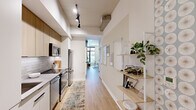 This well-appointed 1-bedroom, 1-floor unit offers a smart and efficient layout that maximizes every square foot. The entrance opens into a galley-style kitchen outfitted with stainless steel appliances, including a range, over-the-range microwave, and dishwasher. Light wood cabinetry, white lower cabinets, and a classic subway tile backsplash give the kitchen a clean, modern aesthetic, complemented by light hardwood flooring that runs throughout the space.

A hallway connects the kitchen and entrance to the rest of the unit, lined with open shelving that adds both storage and visual interest. The living room is a standout, featuring floor-to-ceiling windows that flood the space with natural light and offer views of the surrounding urban streetscape. An elegant arched architectural detail frames the dining nook area, adding character and a sense of depth to the living space.

The bedroom is a serene retreat, highlighted by a bold geometric textured wall accent behind the bed, soft blue-grey painted walls, and a large window that brings in natural light while framing outdoor views. Two closet doors provide ample storage within the room. Light hardwood floors, thoughtful lighting, and a cohesive modern design palette tie the entire space together into a cohesive, comfortable home.