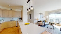 This single-floor residence showcases a thoughtfully designed open-concept layout that seamlessly connects the kitchen and living areas. The kitchen is equipped with stainless steel appliances, including a refrigerator, range, and built-in microwave, all complemented by light wood cabinetry extending to the ceiling for ample storage and clean white countertops. A large island with pendant lighting serves as both a functional workspace and a natural transition into the living area.

The living room is bright and inviting, anchored by a generous sliding glass door that frames expansive city views and fills the space with natural light. Light hardwood flooring runs throughout, lending warmth and continuity across the main living areas.

The two bedrooms each feature large windows with city panoramas, providing an abundance of daylight and an airy feel. The primary bathroom offers a white subway-tiled shower, a quartz-topped vanity with warm wood cabinetry, and light tile flooring. A secondary full bathroom mirrors the clean, modern aesthetic, while a compact half-bath with a pedestal sink serves as a convenient powder room. Overall, the residence presents a cohesive, contemporary design with neutral tones and quality finishes throughout.