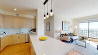 This single-floor residence showcases a thoughtfully designed open-concept layout that seamlessly connects the kitchen and living areas. The kitchen is equipped with stainless steel appliances, including a refrigerator, range, and built-in microwave, all complemented by light wood cabinetry extending to the ceiling for ample storage and clean white countertops. A large island with pendant lighting serves as both a functional workspace and a natural transition into the living area.

The living room is bright and inviting, anchored by a generous sliding glass door that frames expansive city views and fills the space with natural light. Light hardwood flooring runs throughout, lending warmth and continuity across the main living areas.

The two bedrooms each feature large windows with city panoramas, providing an abundance of daylight and an airy feel. The primary bathroom offers a white subway-tiled shower, a quartz-topped vanity with warm wood cabinetry, and light tile flooring. A secondary full bathroom mirrors the clean, modern aesthetic, while a compact half-bath with a pedestal sink serves as a convenient powder room. Overall, the residence presents a cohesive, contemporary design with neutral tones and quality finishes throughout.