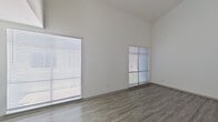 This two-floor residence offers a clean, modern aesthetic defined by crisp white walls, consistent wood-look flooring in a neutral gray tone, and a well-organized layout across both levels. The main living area immediately impresses with its soaring vaulted ceilings, which create a strong sense of openness and volume. Two generously sized windows fitted with horizontal blinds flood the space with natural light, enhancing the bright and airy atmosphere throughout.

The galley-style kitchen is thoughtfully designed, featuring gray shaker-style cabinetry on both sides, light countertops, a stainless steel double sink, subway tile backsplash, and black appliances including a refrigerator, electric range, dishwasher, and over-range microwave. The entry level also includes a functional foyer with a carpeted staircase, interior door access, and a secure front entry.

Upstairs, the space continues with additional rooms finished in the same neutral palette and wood-look flooring. A notable upper-level feature is a tucked storage or bonus area with a sloped ceiling and a built-in ledge, ideal for maximizing use of the roofline space. The bathroom is well-appointed with gray vanity cabinetry, a white countertop, a large mirror, and a lighted vanity fixture. Throughout, the design is clean and move-in ready.