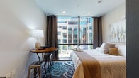 Located in the heart of downtown Hartford, this thoughtfully designed studio at 101 Pearl Street, Unit 203, offers a compelling blend of modern aesthetics and urban convenience. The open-concept layout makes efficient use of space, seamlessly connecting the living, sleeping, and kitchen areas into one cohesive environment.

The sleeping area is a standout feature, anchored by a large floor-to-ceiling window that frames striking views of the surrounding Hartford cityscape. Dark curtain panels frame the glazing, allowing for both abundant natural light and full privacy as desired. A patterned area rug in teal and charcoal adds a bold decorative touch, complemented by a compact bistro-style dining table and industrial metal stools.

The kitchen is outfitted with rich, dark wood cabinetry paired with sleek upper cabinets in a warm taupe finish. Stone-look countertops provide a durable and elegant work surface, while an eye-catching patterned tile backsplash with ornate motifs adds character and depth. Stainless steel appliances and under-cabinet lighting complete the well-appointed culinary space.

The bathroom features large-format light grey floor tiles, a glass-enclosed walk-in shower with matching decorative tile accents, and clean, neutral wall tones that create a calm and spa-like atmosphere. Light wood-tone flooring flows throughout the main living area, tying the space together with warmth and continuity.