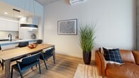 Located at 1555 Boul Chomedey in Laval, QC, this well-appointed one-bedroom, one-bathroom unit offers a thoughtfully designed open-concept layout across a single floor. Light oak hardwood flooring runs throughout, lending warmth and continuity to the space.

The kitchen is a standout feature, outfitted with floor-to-ceiling flat-panel white cabinetry, stainless steel appliances including a full-size refrigerator and dishwasher, and a sleek white quartz island with bar seating. A linear pendant light and matte black fixtures add a refined, contemporary touch. The kitchen flows seamlessly into the dining area, where a warm wood table is anchored beneath a bold circular pendant light, creating an inviting space for meals.

The living area extends naturally from the dining space, featuring a wall-mounted mini-split system and an exposed concrete-panel ceiling that adds an industrial edge to the modern aesthetic.

The bedroom is a calm retreat, bathed in natural light through sheer floor-to-ceiling curtains, with light wood flooring continuing from the main area. The bathroom is elegantly finished with a wood-tone floating vanity, a backlit oval mirror, dark accent wall, large-format tile flooring, and a frameless glass shower with matte black hardware.