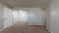 This single-floor unit in Wichita, Kansas, offers a practical and well-organized layout designed for comfortable everyday living. The living area is generously proportioned, finished with neutral gray walls, plush wall-to-wall carpeting, and a textured ceiling. A central partition wall divides the space, creating a defined flow between the main living zone and an adjoining area, with a ceiling-mounted light fixture illuminating the transition.

The galley-style kitchen is efficiently arranged with dark espresso cabinetry lining both walls, white countertops, a stainless steel sink, and tile flooring. White appliances, including a refrigerator and dishwasher, are integrated into the layout, maximizing the available workspace.

The bedrooms are carpeted and painted in soft gray tones, each featuring windows that allow natural light to filter in. Closet space is well-represented, with at least one walk-in closet offering shelving and a hanging rod, and additional bedrooms featuring standard reach-in closets.

The unit includes two bathrooms, both finished with tile flooring and warm wood-toned vanities topped with granite-style countertops. One bathroom features a tub-shower combination, while the other functions as a half bath. Textured walls add subtle dimension throughout the bathrooms, contributing to the unit's consistent, understated aesthetic.