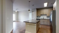Located at 800 Timber Valley Way in Oakwood, Georgia, this single-floor residence showcases a clean, modern design with consistent hardwood-style flooring running throughout the entire space. The open-concept kitchen is a central highlight, anchored by a substantial island with a dark countertop and pendant lighting overhead, offering both prep space and casual seating potential. Light wood cabinetry lines the walls, complemented by a white subway tile backsplash and stainless steel appliances, including a French door refrigerator and built-in microwave. The kitchen flows seamlessly into a generously sized living area bathed in natural light from large windows. The bedrooms feature ceiling fans and windows that provide views of the surrounding neighborhood and greenery. The bathroom is finished with full white subway tile surrounds in the tub-shower combination, brushed nickel fixtures, and wood-style flooring. Neutral gray walls throughout the space create a cohesive, understated palette that complements the warm flooring tones. The overall layout is functional and well-proportioned, offering a bright, move-in-ready environment with thoughtful modern detailing at every turn.