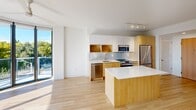Located at 5700 Biscayne Blvd in Miami's vibrant MiMo District, this 2-bedroom, 2-bathroom residence offers a sleek, modern design with an efficient and well-organized layout. Light wood flooring flows seamlessly throughout the entire space, complementing the clean white walls and creating a bright, cohesive aesthetic.

The open-concept living and dining area is anchored by expansive floor-to-ceiling windows and sliding glass doors that lead to a private balcony, flooding the space with abundant natural light and offering refreshing views of Miami's lush tree canopy. The kitchen is outfitted with warm wood cabinetry, white upper cabinets, a tile backsplash, stainless steel appliances, and a substantial island with a white quartz countertop — ideal for both cooking and casual dining.

Both bedrooms feature ceiling fans, large windows or full-height glass doors with outdoor views, and generous closet space. The primary bedroom includes a walk-in closet that connects directly to an en-suite bathroom. The bathrooms are finished in a clean, contemporary style, with the primary bath featuring a glass-enclosed shower, a wide vanity with an illuminated mirror, and refined fixtures. The second bathroom maintains the same polished aesthetic.