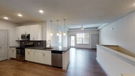 This single-floor residence showcases a thoughtfully designed open-concept layout that seamlessly connects the kitchen and living areas. The kitchen is a standout feature, outfitted with crisp white cabinetry, dark granite-style countertops, and a striking hexagonal mosaic tile backsplash. Stainless steel appliances — including a refrigerator, electric range, over-the-range microwave, and dishwasher — provide a polished, modern aesthetic. A peninsula with pendant lighting overhead serves as both a functional workspace and a natural divider between the kitchen and the open living area. Rich wood-tone flooring runs throughout the main living spaces, complementing the neutral white walls and tray ceiling detail accented by a ceiling fan. Natural light flows in through large windows, brightening the generous living area. The bedroom features soft wall-to-wall carpeting, a tray ceiling with ceiling fan, a large window with exterior views, and a wide reach-in closet with double hanging rods. The bathroom is finished with wood-look tile flooring, a full soaking tub, and floor-to-ceiling linear tile surround in warm beige tones. The overall ambiance is clean, contemporary, and move-in ready.